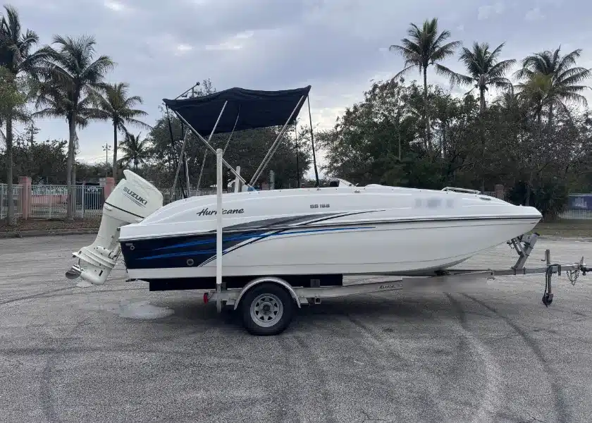 A white deck boat with a bimini top on its trailer in front of palm trees