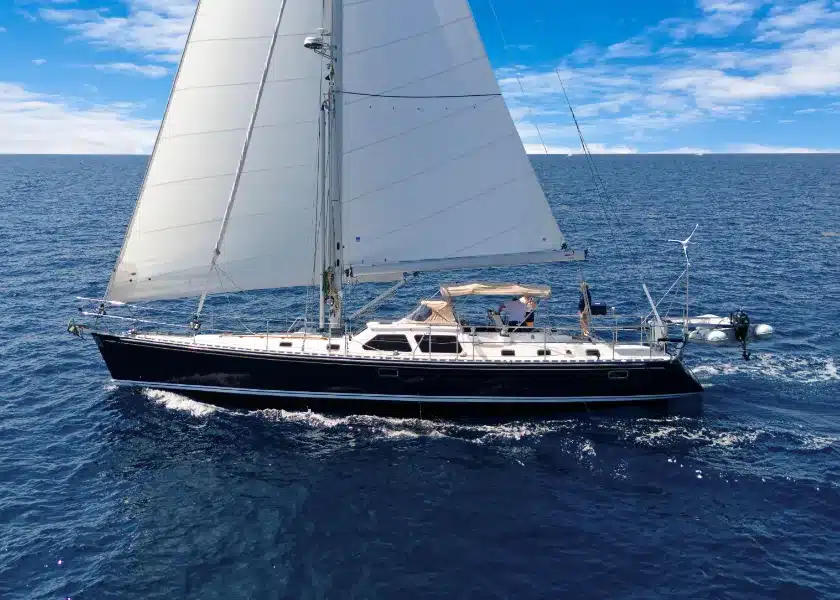 A dark-hulled cruising sailboat under sail on open blue water off Fort Lauderdale