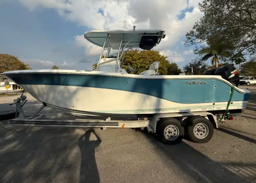 A teal and white center console boat on its trailer in a parking lot