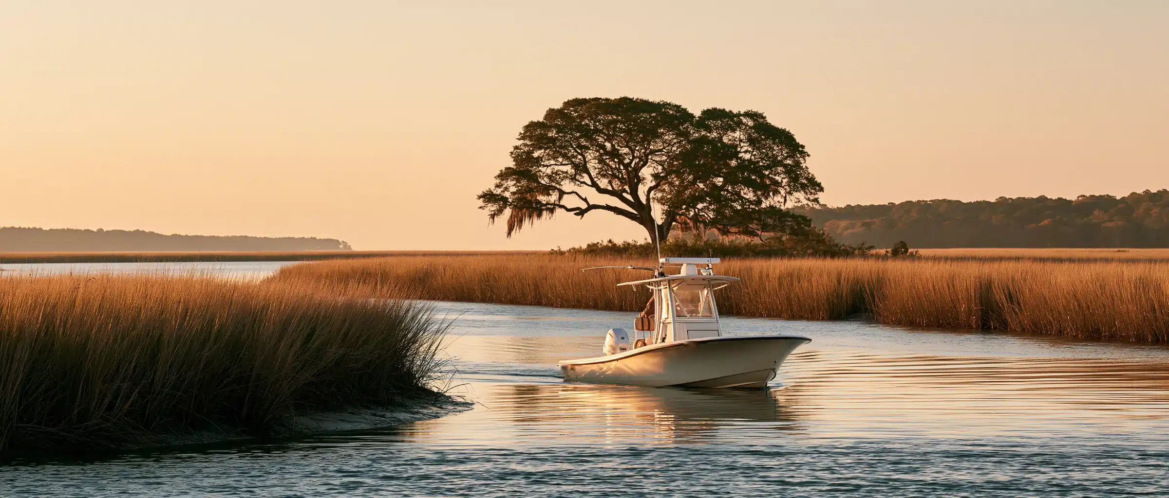 A center console boat with a T-top running a tidal creek past golden cordgrass and a live oak draped in Spanish moss