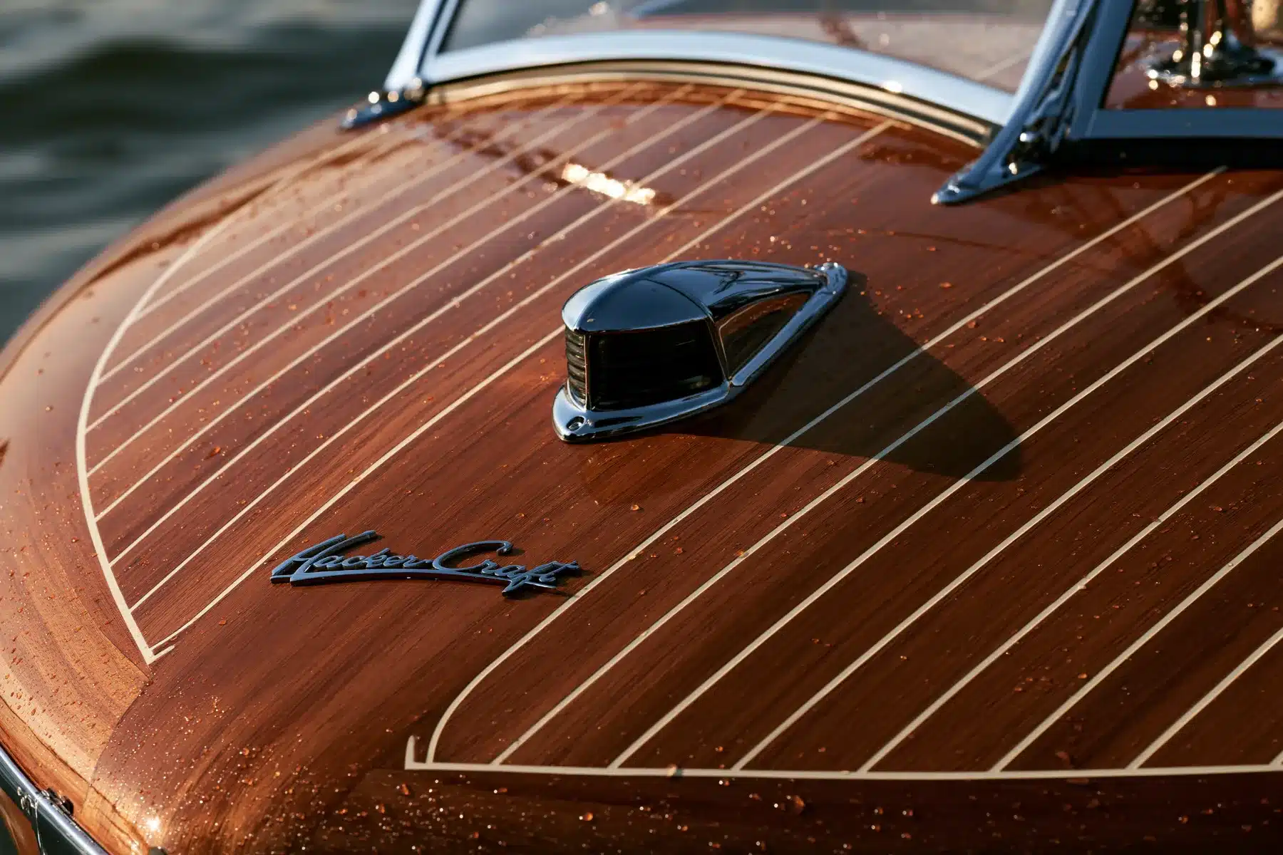 Close view of the varnished mahogany foredeck of a restored Hacker-Craft runabout, with a chrome bow light, the Hacker-Craft script badge and cream deck seams