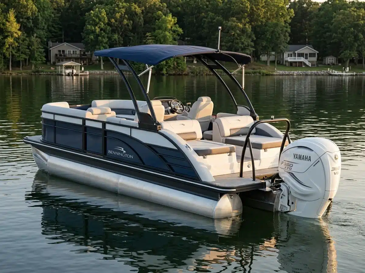 A navy and white luxury tritoon with a bimini top and a white Yamaha V8 outboard idling on a calm wooded lake at golden hour